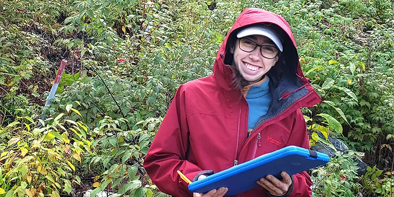 Maria standing in brush with clipboard