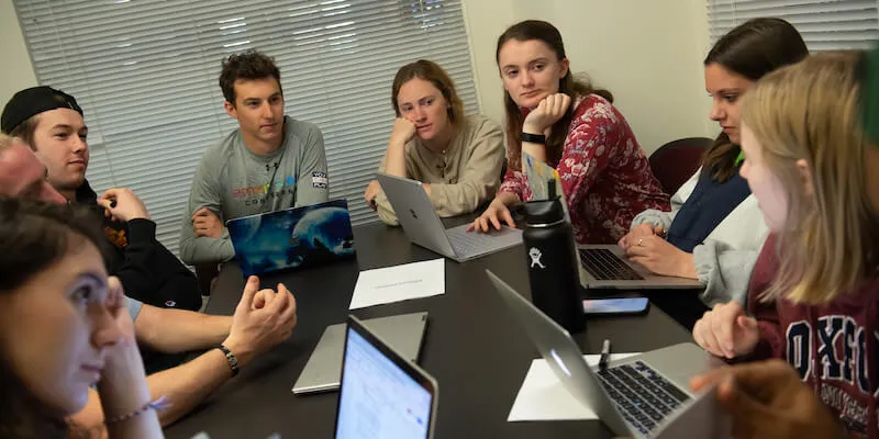 Students engage in discussion around a classroom table.