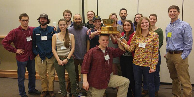 Group of students and faculty displaying Quiz Bowl trophy
