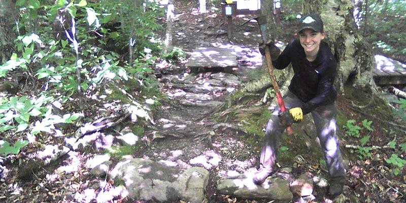 Sarah Drew swinging a pick axe on a hiking trail