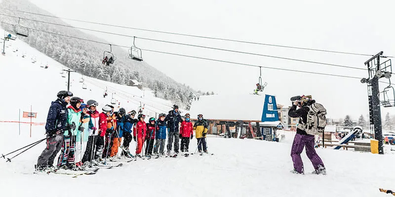 Hilary Byrne films group of skiers at the base of a mountain.