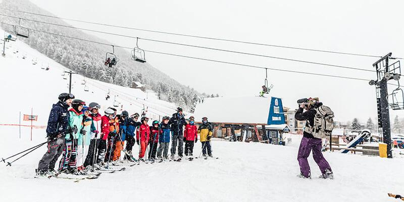 Hilary Byrne films group of skiers at the base of a mountain.