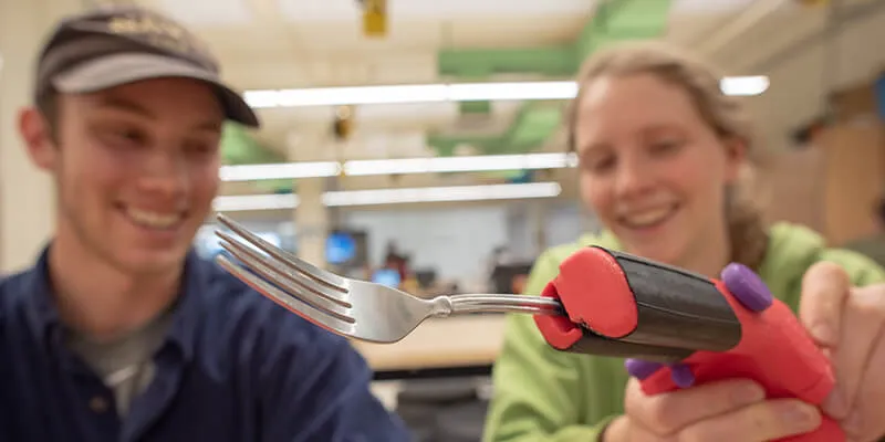 Two University of Vermont students with a 3D printed device holding a fork