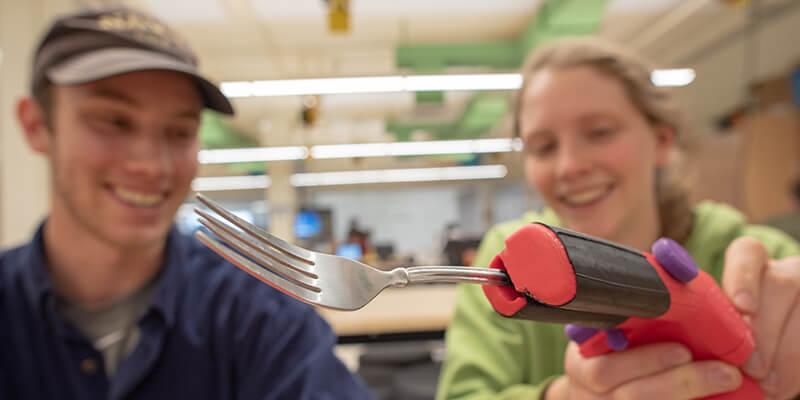 Two University of Vermont students with a 3D printed device holding a fork
