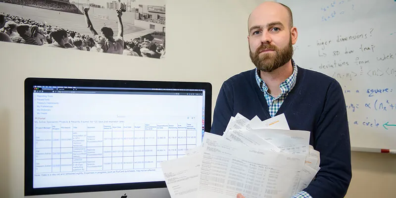 Adrian DelMaestro holding a stack of papers in front of a computer screen
