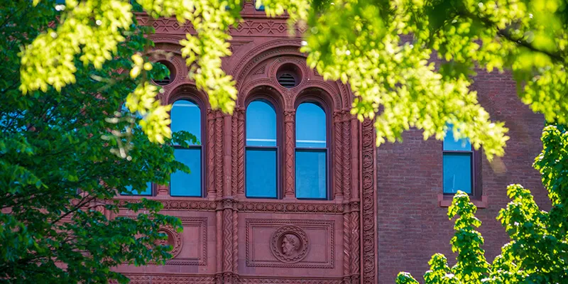 Red brick windows on Williams Hall behind green tree branches