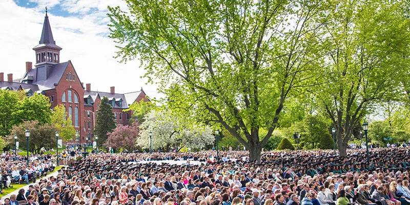 Graduates sit on the UVM Green in front of Old Mill