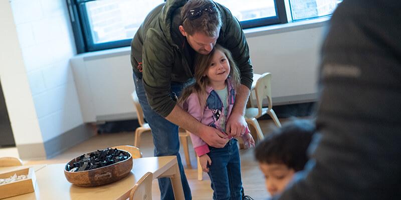 Father zipping up jacket on daughter at daycare