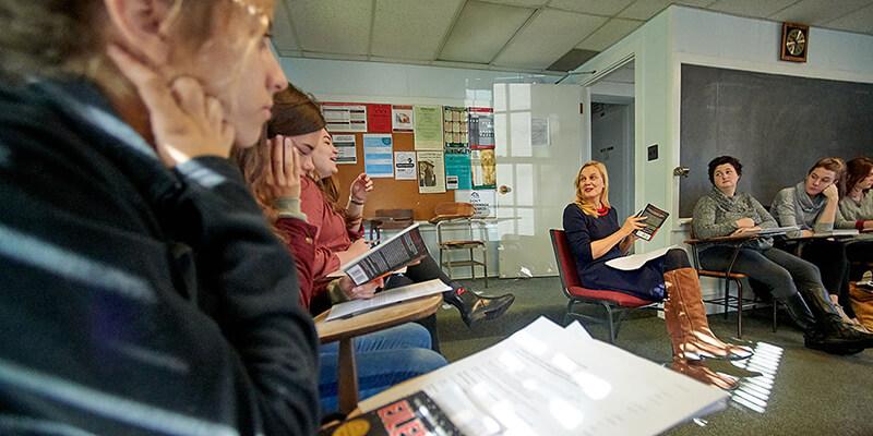 Students sit at desks in a circle in a classroom around professor Maria Hummel