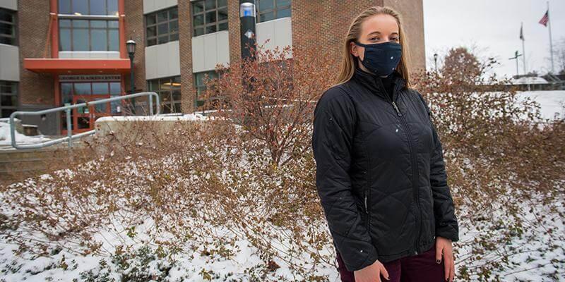 Student Izzy Coppola stands in front of UVM's Rubenstein School in snow