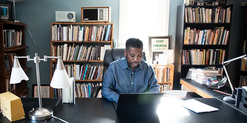 UVM professor of English Major Jackson writes at his computer in home office
