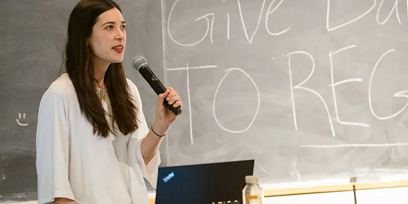 Mariel Golden holds a microphone in front of a chalkboard