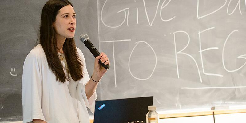 Mariel Golden holds a microphone in front of a chalkboard