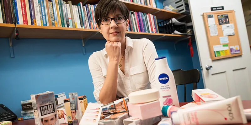 Professor Nikki Khana sitting at her office desk with a pile of whitening creams in front of her.