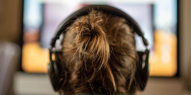 girl wearing headphones staring at computer screen, seen from behind
