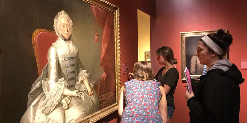 Three students examine a portrait in a museum