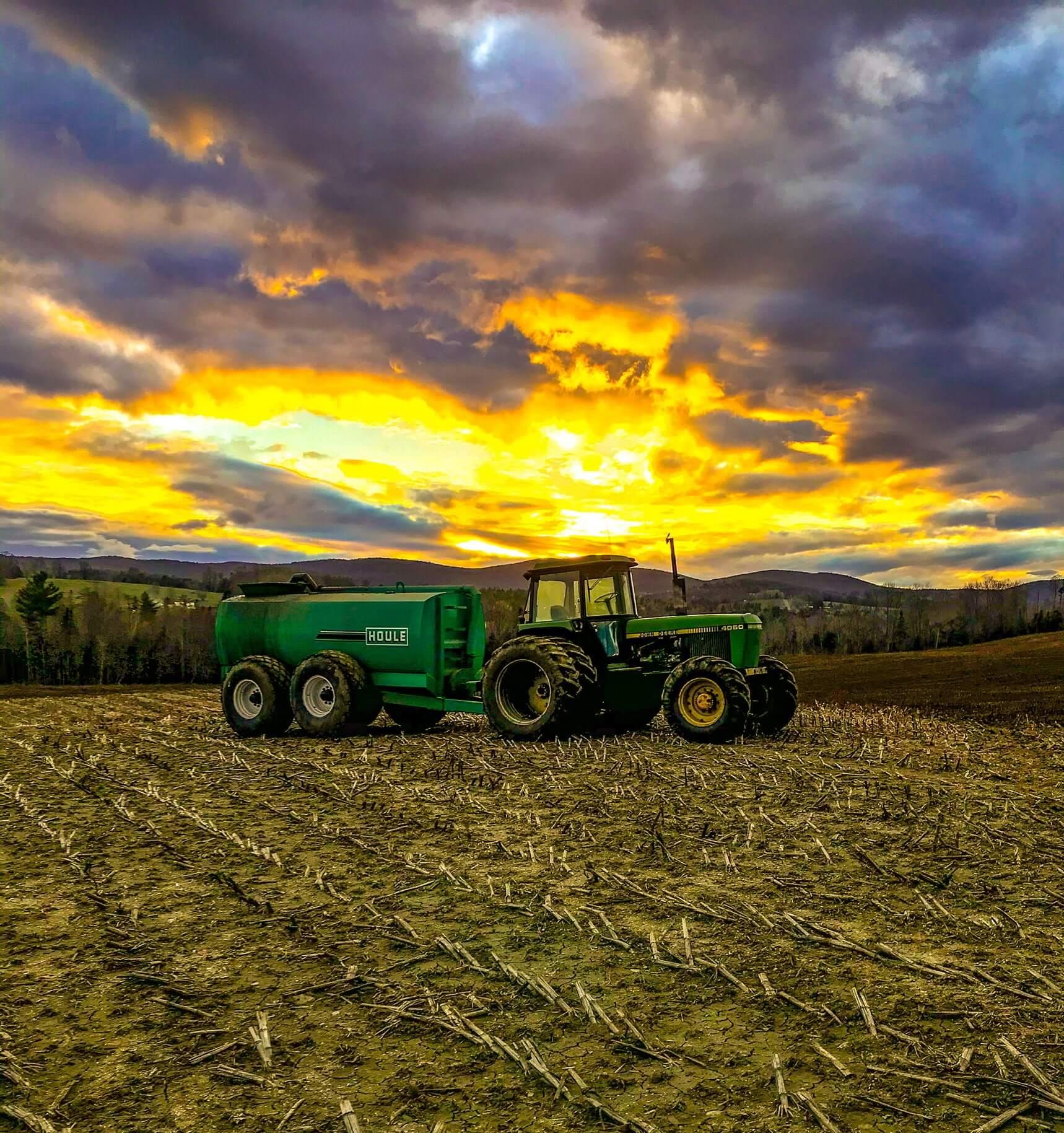 A tractor in a field with a sunrise behind