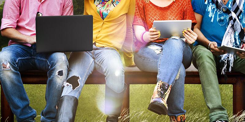 Laptops sit on legs of four individuals sitting on bench