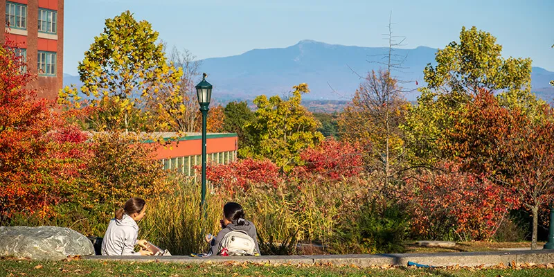 two students sit in outdoor amphitheater with Mount Mainsfield in the distance