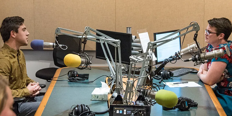 A science student sits opposite Vermont Public Radio host Jane Lindholm, talking into microphones in a studio.