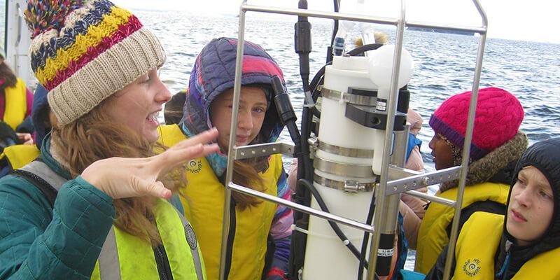 College student shows three middle school students equipment on a research vessel