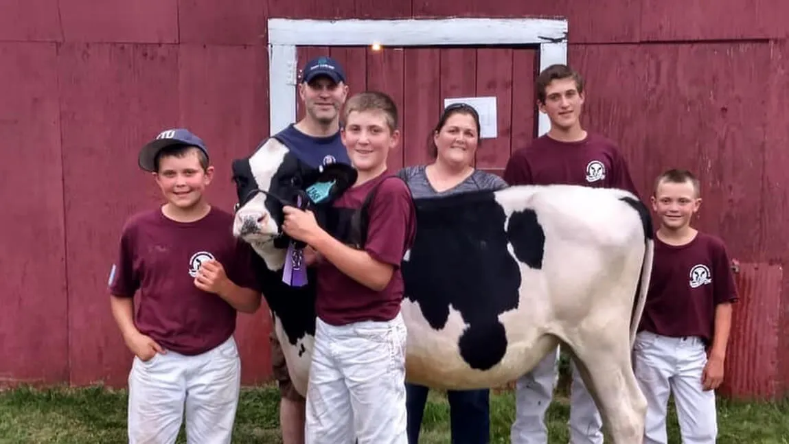 6 people with a black and white holstein cow in front of a red and white barn