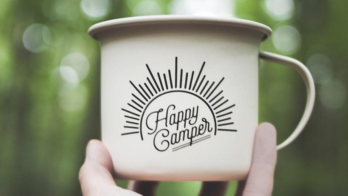 Hand holding a mug that says 'happy camper' on it