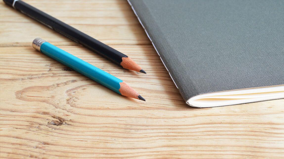 two pencils with an exam booklet on a wood desk