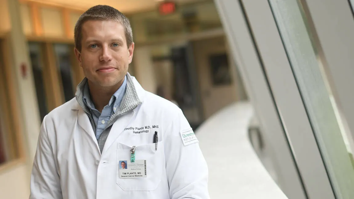 Tim Plante '06 posing in white UVM lab coat