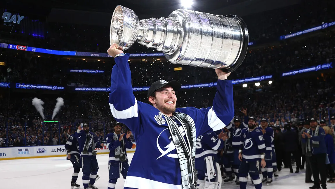 Ross Colton hoists the Stanley Cup Trophy overhead on the ice rink