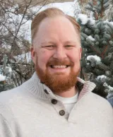 A man with red hair and a red beard wearing a tan sweater