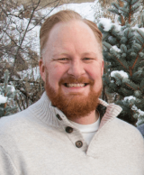 A man with red hair and a red beard wearing a tan sweater
