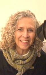 A woman with White hair wearing a green scarf and a black sweater
