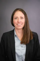 A woman with brown hair wearing a black suit with a blue shirt