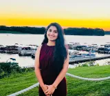 A woman with black hair in a red dress standing in front of a harbor 