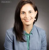 A woman with brown hair wearing a blue jacket with a teal shirt below 