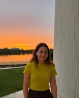 A woman with light brown hair wearing a yellow shirt in front of a sunset 