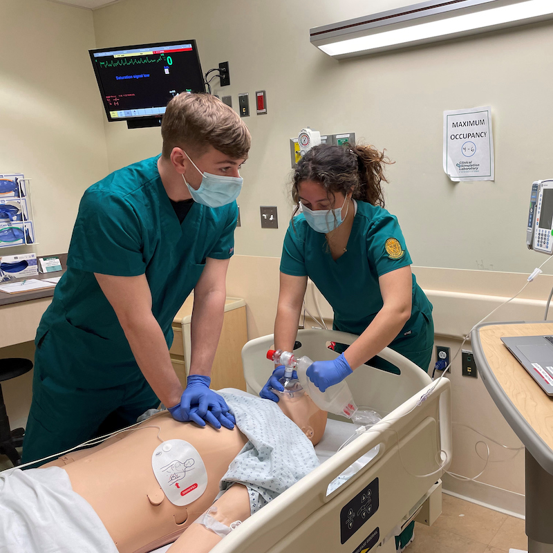 Two nursing students practice CPR on a dummy.