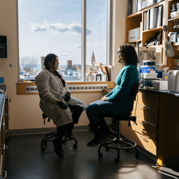 Two people sitting in a lab, facing each other with a window in the background