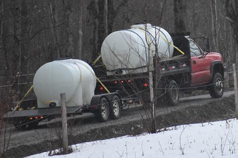 Pickup truck and trailer hauling sap in large white containers