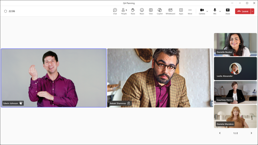 A screenshot of a Microsoft Teams meeting showing two signing participants in large tiles, with other participants to the side. The signing participants have symbols next to their names indicating their role as a signer or interpreter.