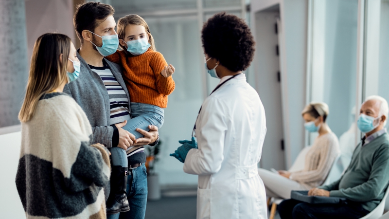 Young family wearing face masks while talking to a doctor in the hospital.