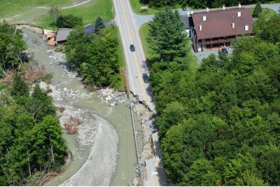 Winding river cutting into road with houses and trees
