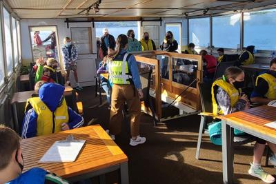 Middle School students at tables inside a boat with a lake outside the windows