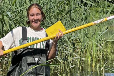 Student in waders stands in pond with long instrument.
