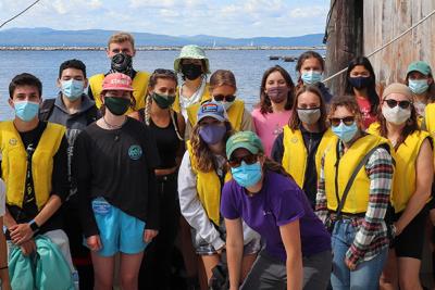 Group of 20 people in masks and life vests on a boat at a lake dock