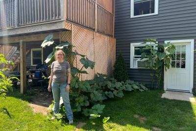 Gretchen standing in a yard with a large squash plant