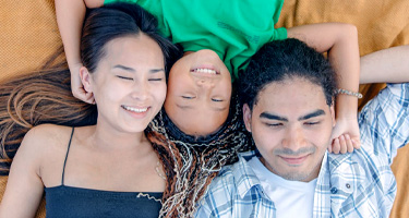 mother father and daughter laying down next to each other and smiling