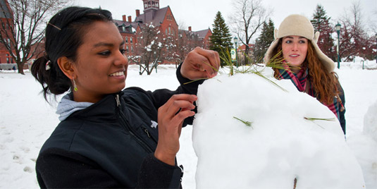 A student builds a snowman on the campus green