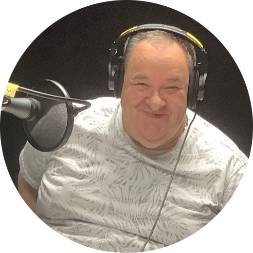 A smiling white man in his sixties, wearing headphones and seated in front of a microphone